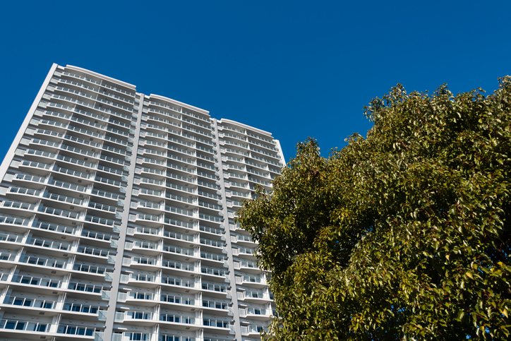 High rise condominium in Yokohama, Japan. Low angle view of the white building against blue sky. There are green trees in front of the structure.
